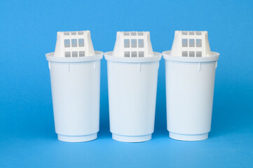 Three new filter cartridges for water purification stand in a row on blue background, close-up....