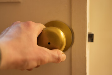 A man's hand opening a white door with gold handle. Security concept - obrazy, fototapety, plakaty