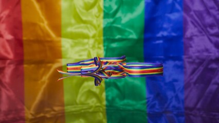 Rainbow color ribbon reflects on glass surface with Gay and LGBT flag in the background