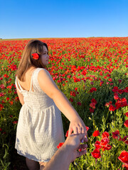 A man holds a woman's hand in a poppy field