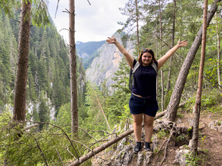 Girl traveler standing by a cliff in a coniferous forest