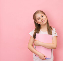 Smiling schoolgirl  holding copy-books on pink background with copy space. Education and back to school concept.