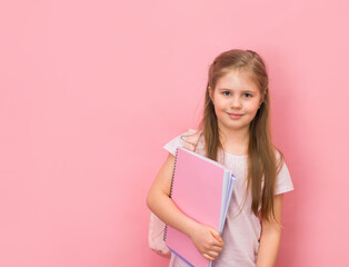 Smiling schoolgirl with backpack holding copybooks on pink background. Mock up on pink background. Education concept.