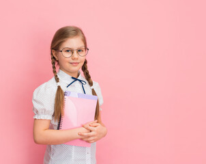 Smiling schoolgirl in eyeglasses holding copybooks on pink background. Mock up on pink background. Education concept.