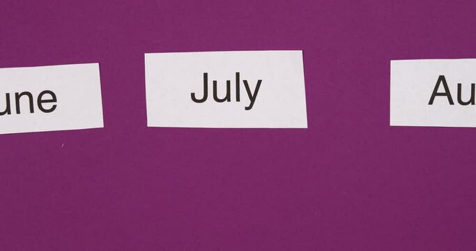 Month names changing on purple paper background. Time passing, calendar, seasons concept. Top view, 4K stop motion animation.