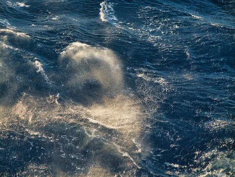 Spray over breaking waves at sea in sunlight.