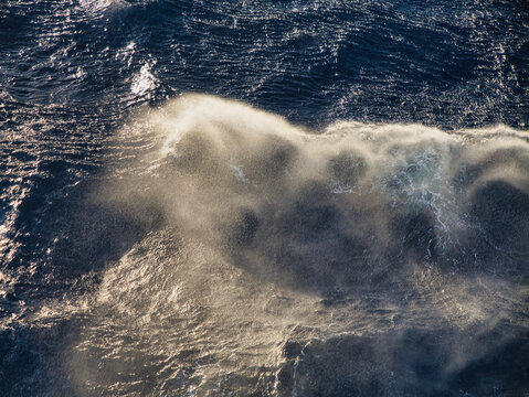 Spray over breaking waves at sea in sunlight.