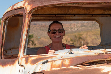 South Africa. 16/02/2024. Attractive woman posing with an old rusty American car on the roadside in...