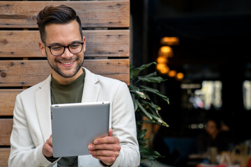 Handsome standing outdoors during the day and using digital tablet for work. Focused guy with...