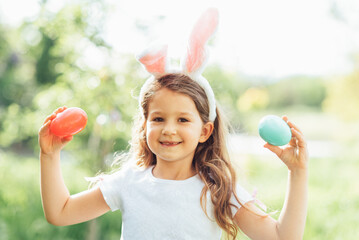 Cute funny girl with Easter eggs and bunny ears at garden. easter concept. Laughing child at Easter egg hunt. Child in park with basket full of eggs, spring concept