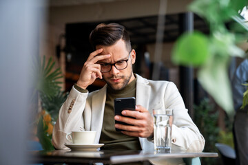 Shot of a handsome young businessman looking thoughtful while scrolling on his mobile phone at...