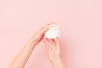 Round jar of cosmetic cream in hand on pink background. Cosmetics beauty mockup for product branding