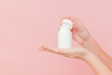 White bottle plastic tube in woman's hands on pink background. Packaging for pills, capsules or supplements. Cosmetics