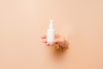 White bottle with serum lotion or essential oil (hyaluronic acid and collagen) in hand on beige...