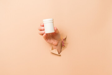 Cool view on white bottle plastic tube in hands on beige background. Packaging for pills, capsules, supplements or ointment. Cosmetics