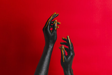 Black and gold colors painted woman's hands on her skin with red background. High Fashion art concept - obrazy, fototapety, plakaty