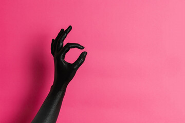 Black painted elegant woman's hand on her skin gesticulates on pink background. High Fashion art...