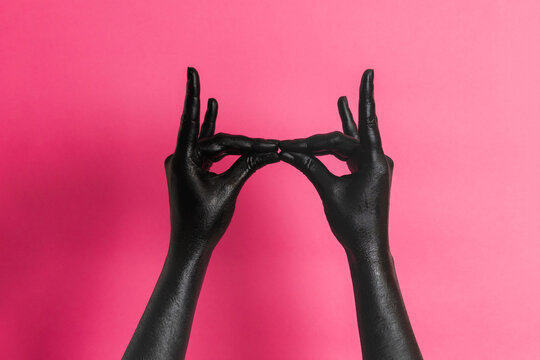 Black painted elegant woman's hands on her skin gesticulate on pink background. High Fashion art concept