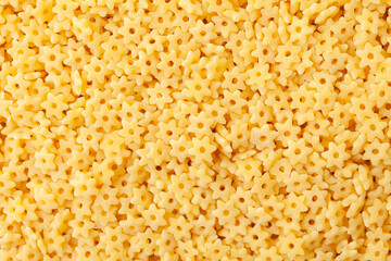 Uncooked yellow small stars shaped pasta background. Top view