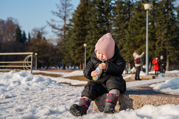 Fototapeta na wymiar A small child girl drinks kefir in a cardboard box outside in winter in the park. Saint Petersburg, Russia - 9 March 2024