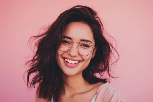 Portrait of a smiling young woman in glasses against pink background.