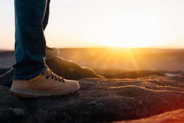 closeup of feet of man in special boots walking in the mountains reaching the destination and on the top of mountain at sunrise or sunset. Travel Lifestyle concept - obrazy, fototapety, plakaty