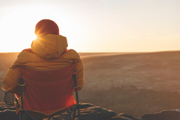 A woman in an yellow jacket relaxing alone on the top of mountain  at sunrise or sunset on spring cold day. Travel  Lifestyle concept
