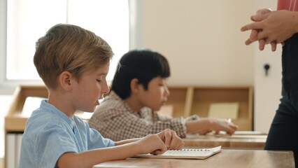 Side view of caucasian elementary student looking a note and answer question while sitting in front...