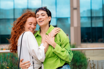 Fototapeta premium smiling young women girlfriends having a fun time together, talking and using phones, shopping outdoor in an urban city. People, communication, friendship and lifestyle concept