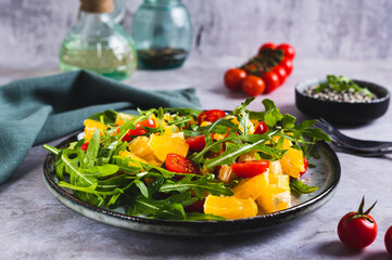 Homemade salad of orange, cherry tomatoes and arugula on a plate on the table