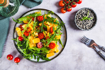 Homemade salad of orange, cherry tomatoes and arugula on a plate on the table top view