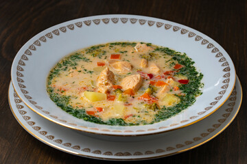 Fresh creamy salmon fish soup with potatoes, carrots, broccoli, peppers and onions in a ceramic plate on a wooden table, closeup. A delicious dinner consists of fish soup with salmon