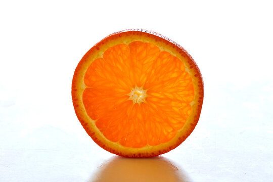 Closeup of an orange slice resting on a white surface in an artistic textured and graphic circle