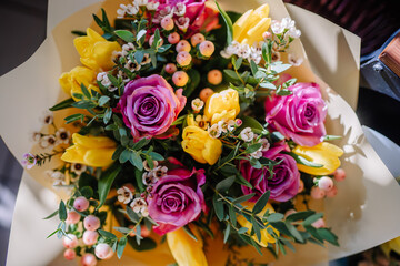 Valmiera, Latvia - March 7, 2024 - A vibrant bouquet of yellow tulips and pink and purple roses, mixed with greenery and small white flowers, wrapped in beige paper.