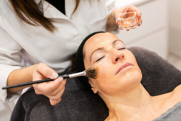 Crop beautician applying cream on face of client