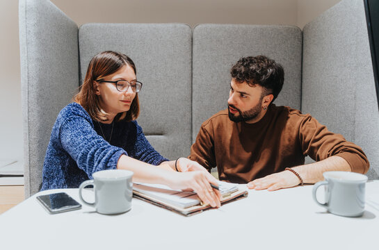 Two focused people analyze documents during a collaborative effort at a modern workplace, with mugs and mobile phone on the table, depicting teamwork and problem-solving.