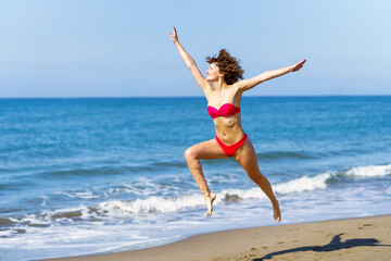 Carefree woman in swimwear jumping on beach