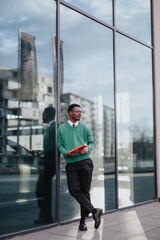 A smartly dressed young male professional walks confidently with a tablet in hand alongside a glass facade in an urban setting.