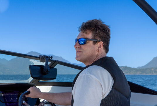 Middle-aged man with sunglasses driving a boat on a summer day at the lake.