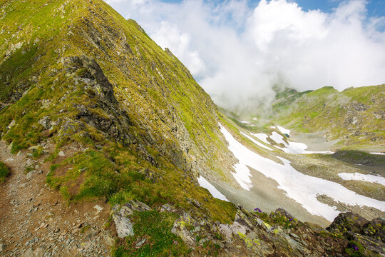 landscape of transylvania alps in summer. spots of snow among grass on the rocky hills of fagaras range beneath a sky with clouds. popular travel destination in the mountains of romania