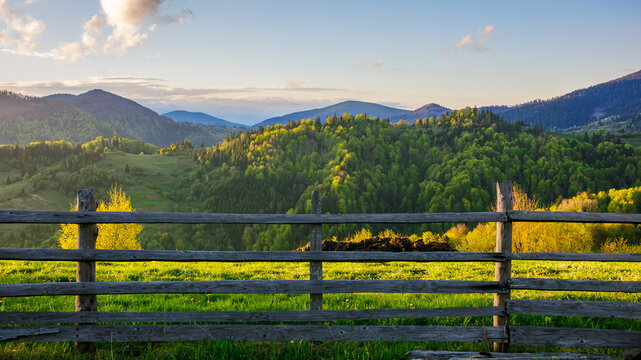 weathered wooden fence. mountainous rural landscape of transcarpathia, ukraine in spring. carpathian countryside with forested rolling hill beneath a blue sky with  fluffy clouds on a sunny evening