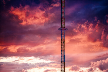 A solitary tower ride pierces the sky, silhouetted against a striking canvas of sunset hues,...