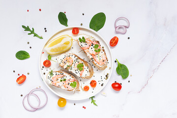 Bruschette set with shrimps, cream cheese and lemon on white marble plate top view