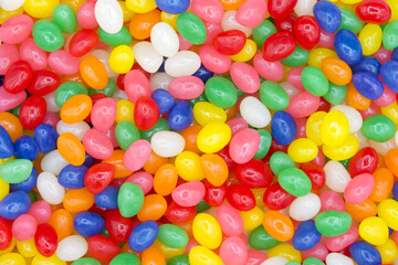 Close up on background of bright vibrant colorful jelly beans, wood spoon comes in and scoops up some candy.