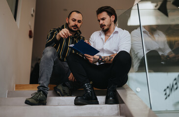 Fototapeta na wymiar Two stylish men reviewing documents together on staircase indoors.
