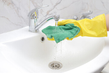 Water flows from the tap onto a cleaning cloth. hand in rubber gloves does wet cleaning in the bathroom. housework and housekeeping concept