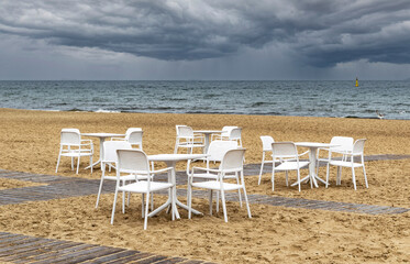 White lounge chairs and table on the sandy beach	with stormy sea