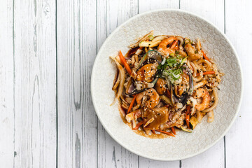 Asian udon noodles with mussels, prawns and vegetables on white wooden background 