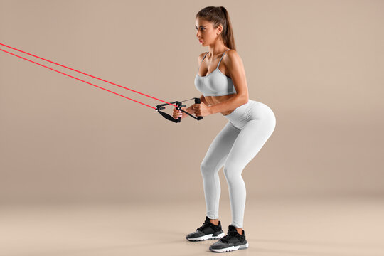 Athletic girl working out with resistance band on beige background. Fitness woman doing exercise