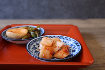 赤いお盆にのせたの皿に盛り付けた蕪のキムチと大根キムチ